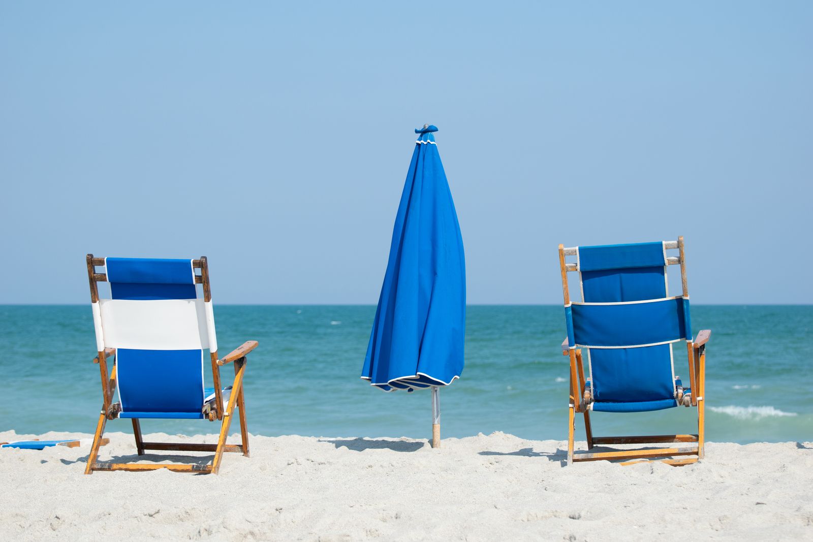 Two blue beach chairs and a blue umbrella facing the ocean, photographed by Mike Loerop
