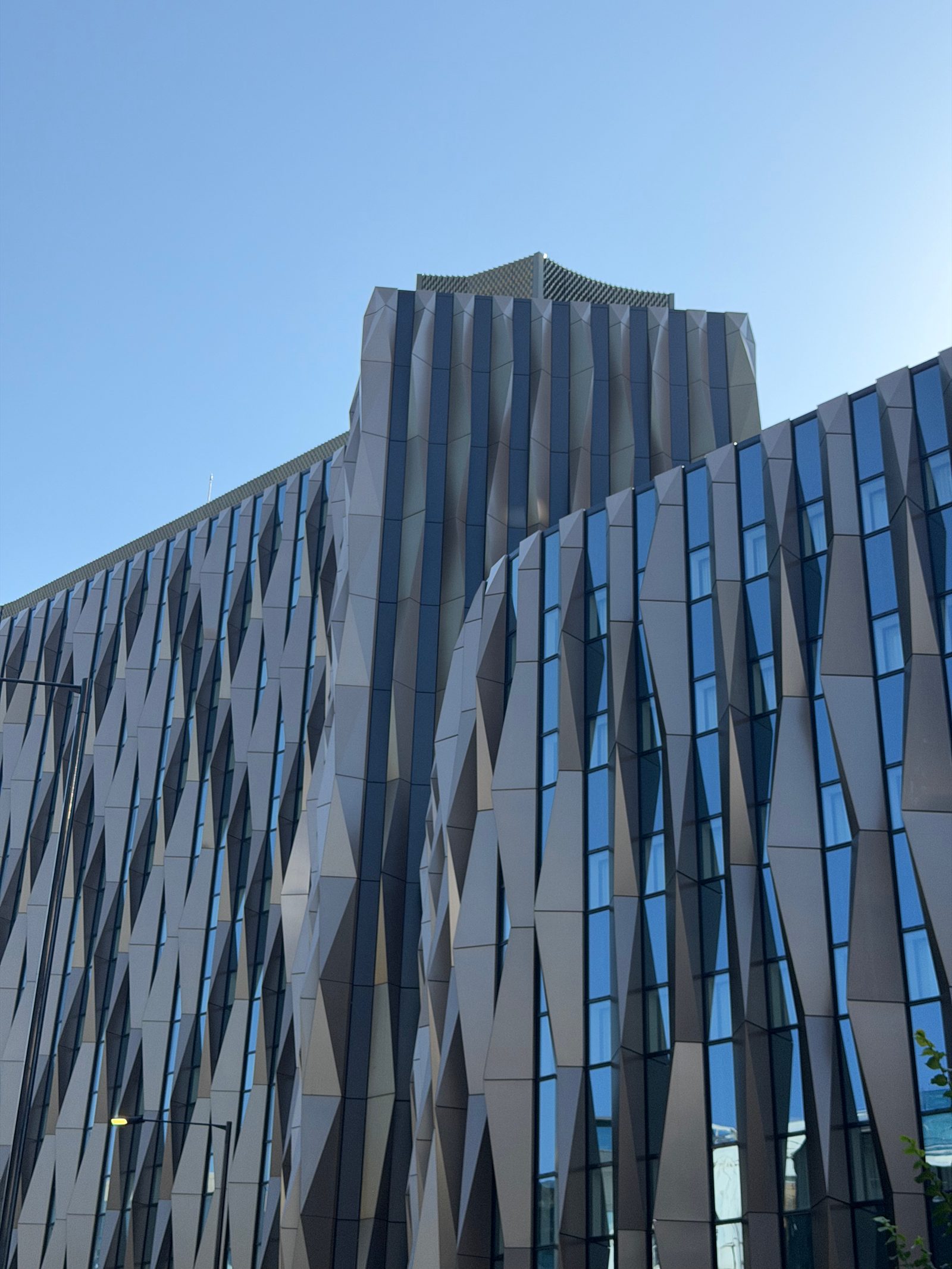 A folded metal and glass building facade against a clear blue sky in London, photographed by Mike Loerop