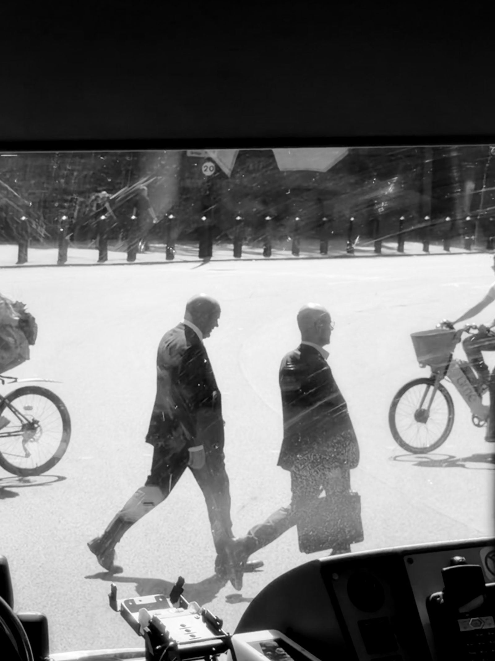 Black and white photo of two men in suits crossing a London street, seen through a bus windshield, photographed by Mike Loerop