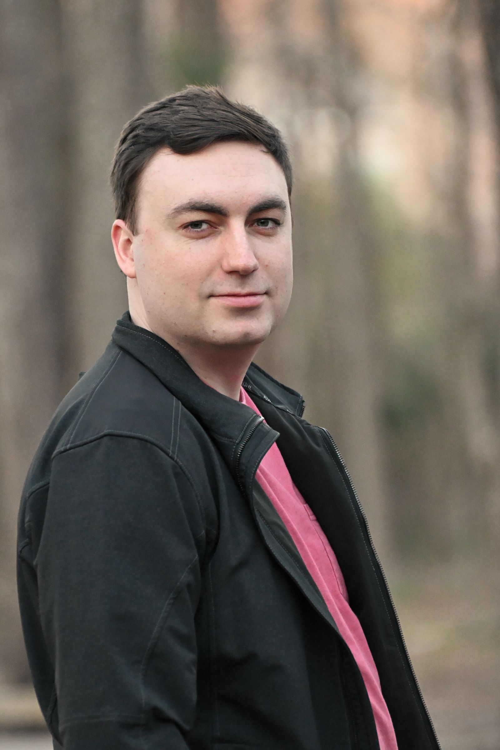 Mike Loerop in a black jacket, smiling softly among the trees